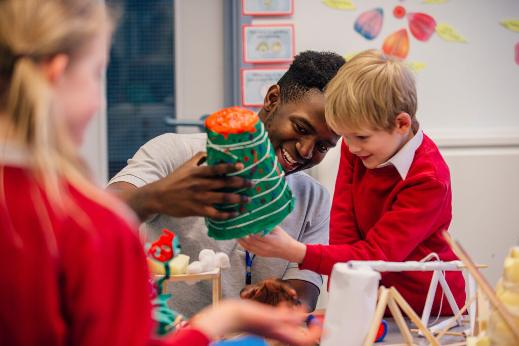 Young teacher is helping one of his primary school students during arts and crafts lesson.