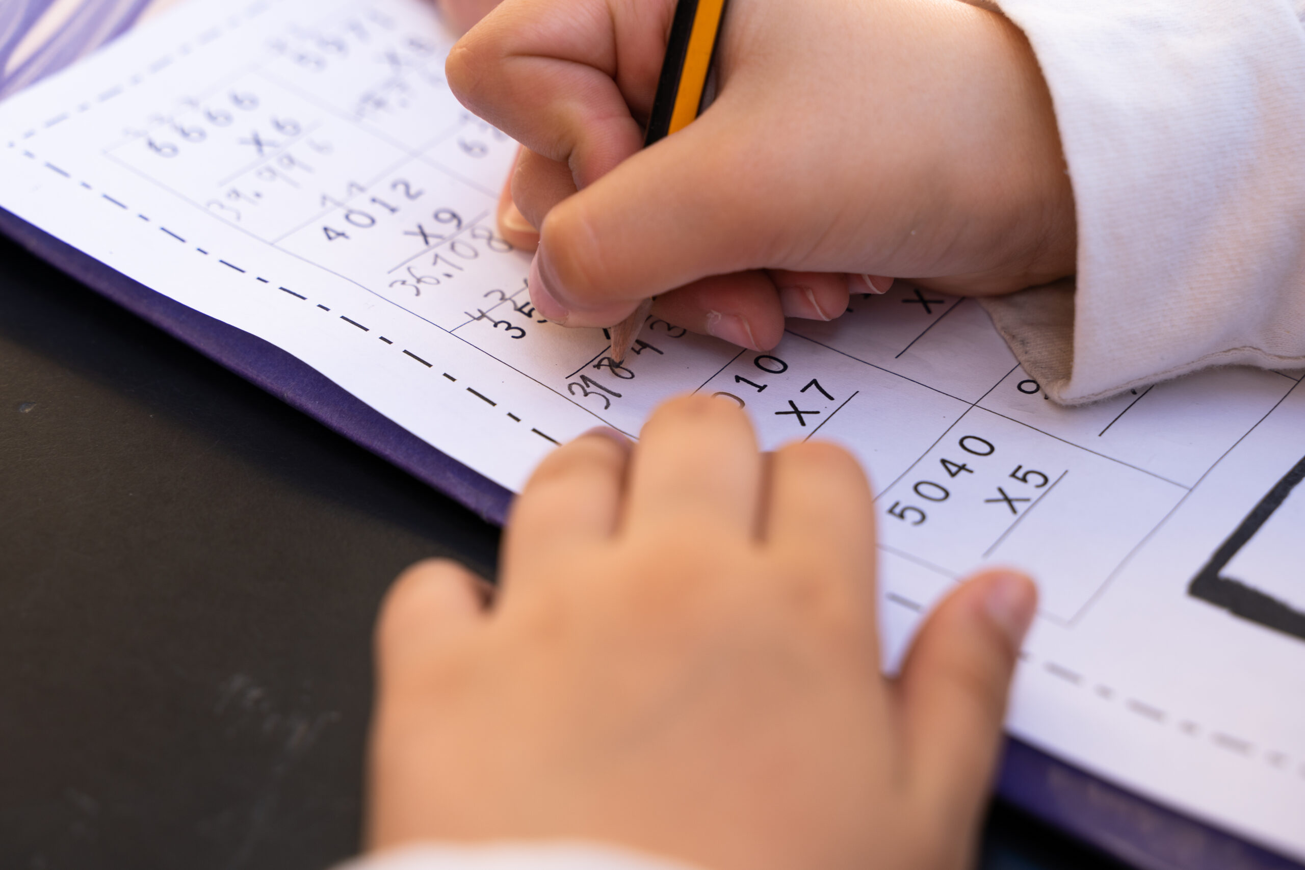 Close up on little girl hands doing school homework. Student writing with pencil maths multiplication exercise sheet